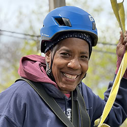 Jennifer Raymond smiles outdoors wearing a helmet and harness for a zip line