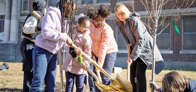 Department of Conservation and Natural Resources Secretary Cindy Adams Dunn plants a tree with four students in front of a school.