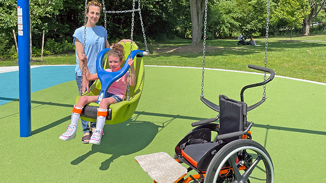 Young child with parent with harnessed chair swing at playground