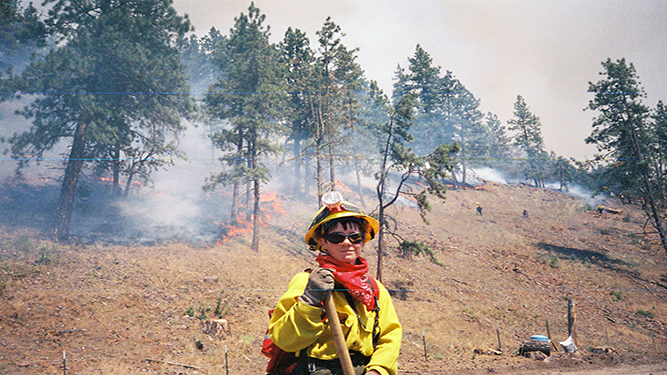 A firefighter stands in front of a forest fire.