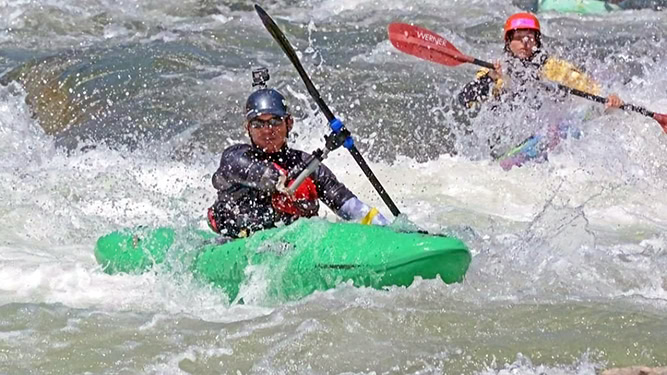 Two kayakers paddling down rough waters.