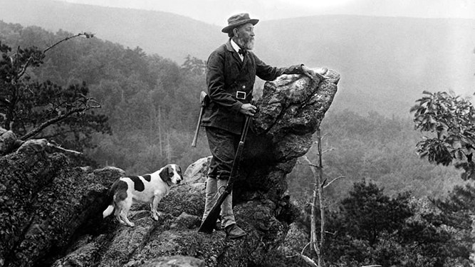 Old black and white photo of Joeseph Rothrock leaning on Pulpit Rock with his small dog standing behind him
