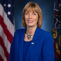 Official Portrait of DCNR Secretary Cindy Adams Dunn wearing blue suit in front of American and Pennsylvania flags.